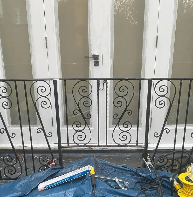 Black steel railings with scroll panels in front of white French doors