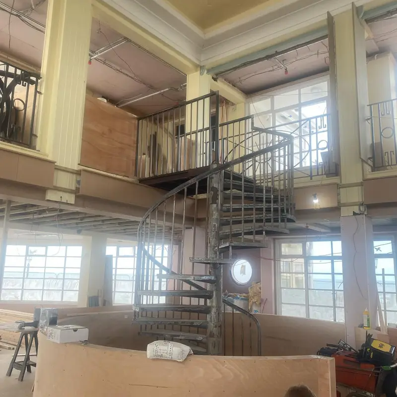 Spiral staircase rising to a railed mezzanine inside a building under refit